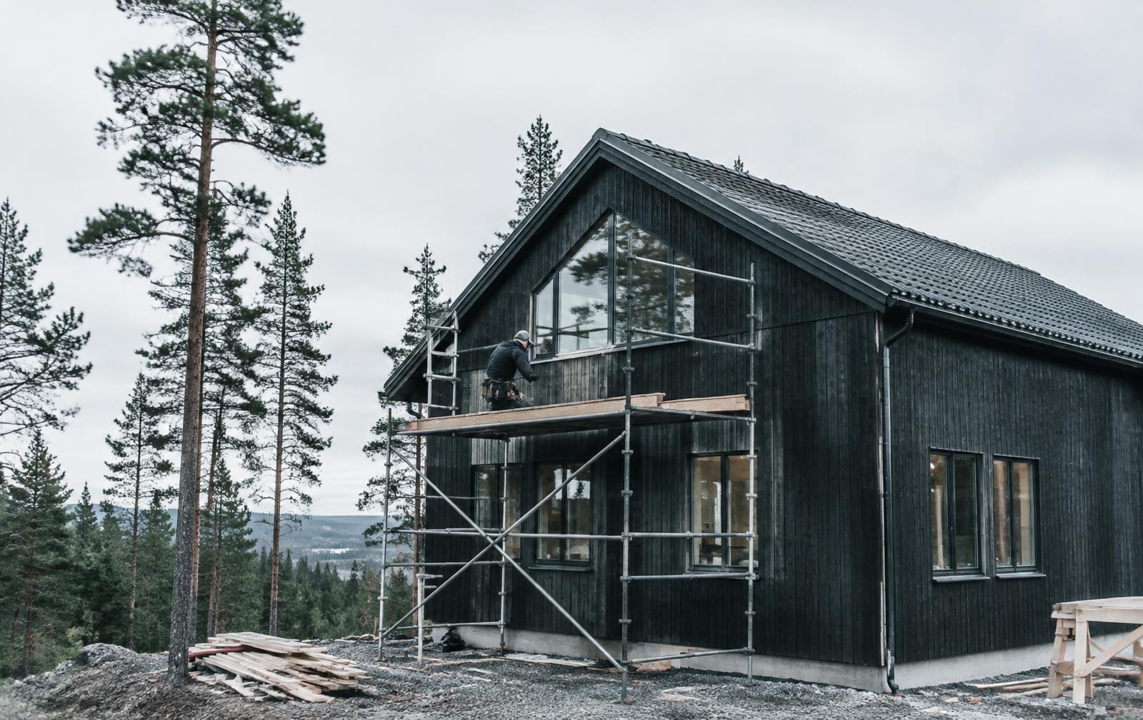 Hantverkare monterar fasadpanel på ett nybyggt svart trähus i Dalarna